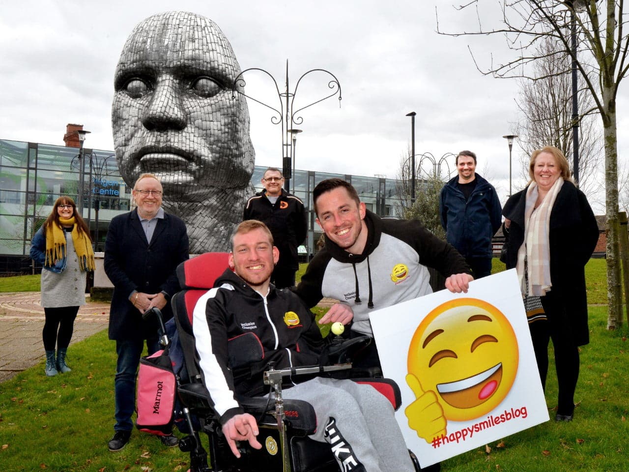 Local social entrepreneurs gathered by the Wigan Face sculpture in the town centre, holding a #happysmilesblog sign