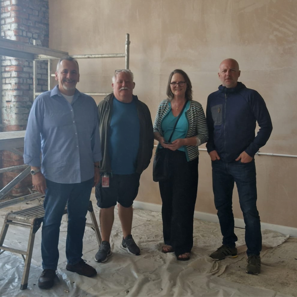 Four members of the Verve team standing in a room mid-refurbishment, with dust sheets across the floor