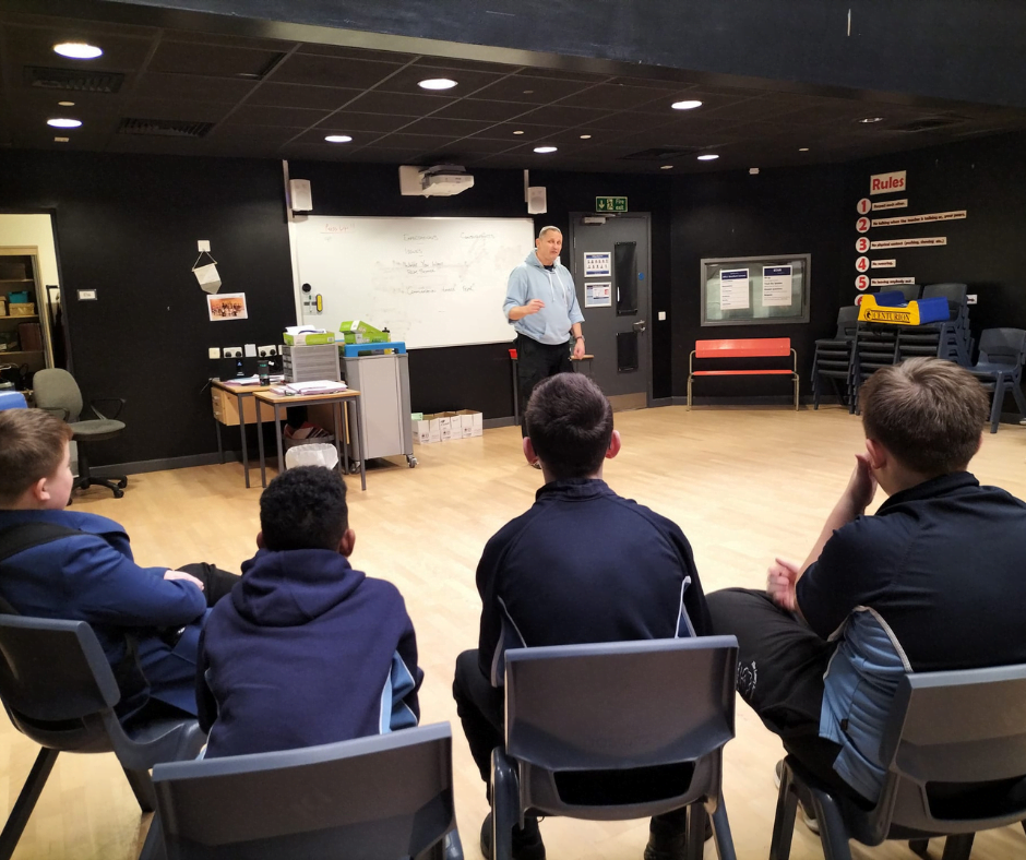 A group leader talking to four secondary school pupils seated in a semicircle during a Verve workshop