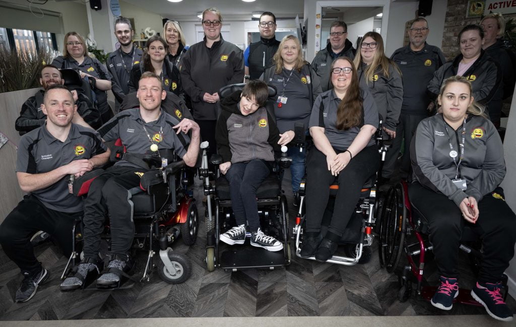 The Happy Smiles team in branded grey uniforms, several of them wheelchair users, gathered for a group photo