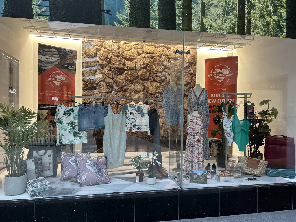 The Rebuild With Hope shop window in the Grand Arcade, dressed with clothing, homeware and branded banners