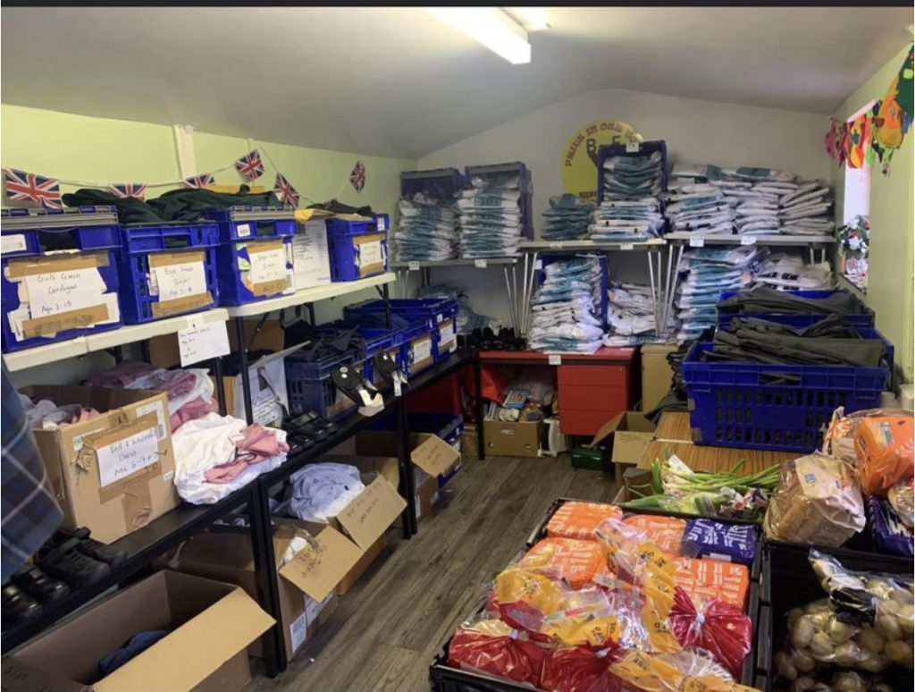 The uniform bank and pantry store room, with school uniform stacked on shelves beside crates of fresh fruit and vegetables