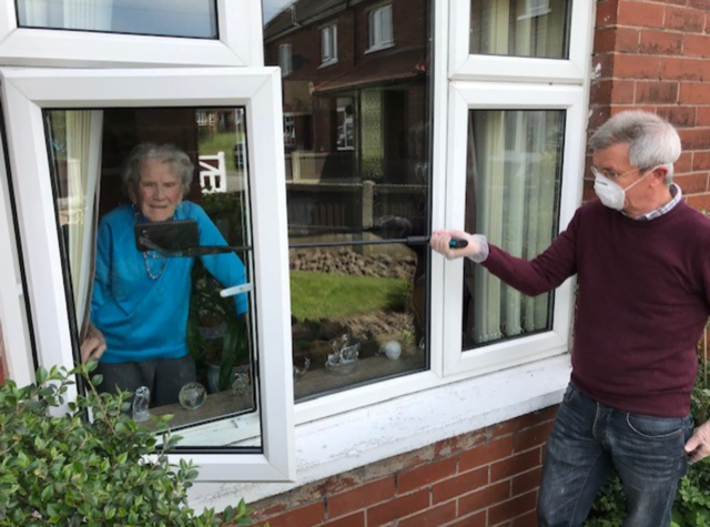 A volunteer in a face mask passing something through an open window to a resident during doorstep support