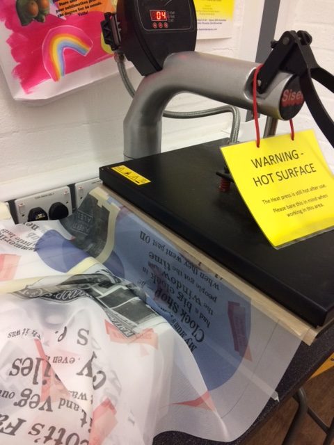 A heat press marked 'Warning – hot surface' transferring the community artwork onto fabric