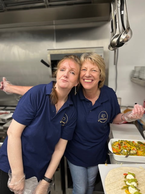 Two café team members preparing trays of food in the kitchen