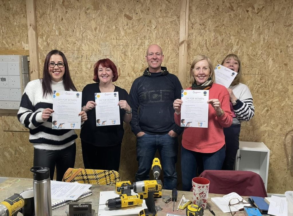 Participants on the DIY for Women course holding their certificates in the workshop, with drills on the bench